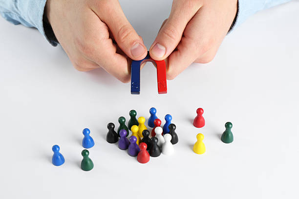 istock Man with magnet attracting game pieces at white table, closeup 2230120719