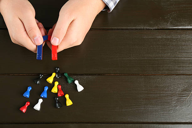 Man with magnet attracting game pieces at wooden table, above view. Space for text