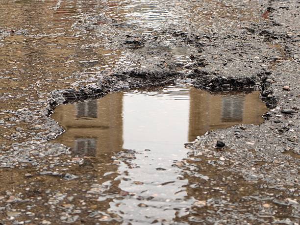 istock A water-filled pothole on a road reflects a building's facade. 2230121911