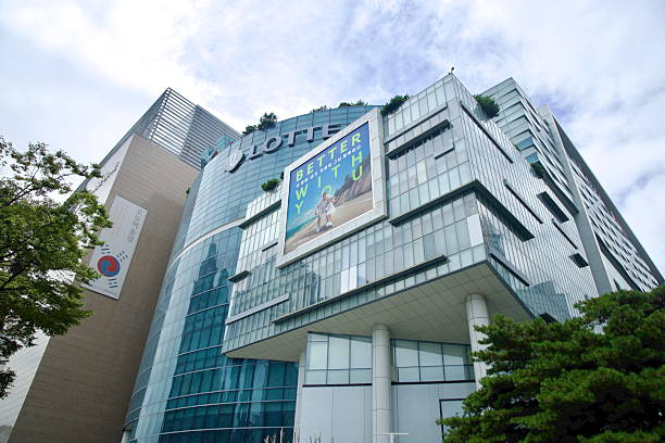The glass and metal facade of Lotte Department Store towers over Centum City, with a large seasonal billboard and planted terraces set against patches of blue sky.