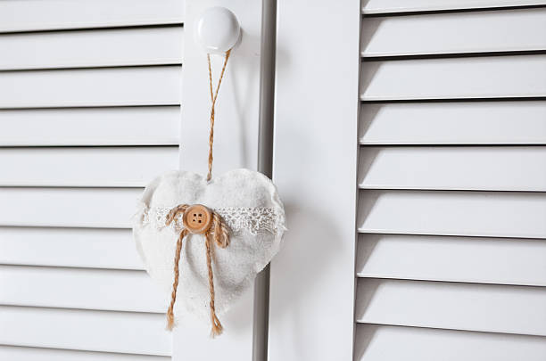 Fabric heart ornament with lace and a wooden button hangs by a string from a white cabinet knob. Soft tones and simple design create a cozy, rustic decorative accent