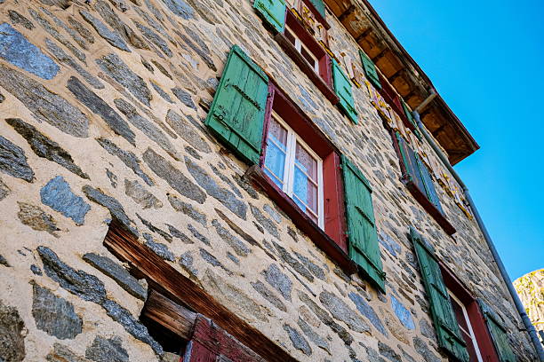 Very old stone building with open wooden window blinds or shutter. Low, wide angle view, no people
