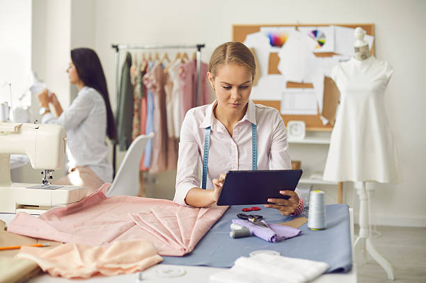 istock Female dressmaker sitting at table in her sewing atelier and using modern tablet 2230135886