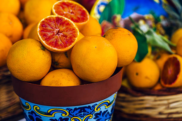 A vibrant display of oranges and blood oranges in a decorative pot, evoking freshness and Mediterranean flavors. Captured in a colorful street market setting, highlighting local and natural produce.