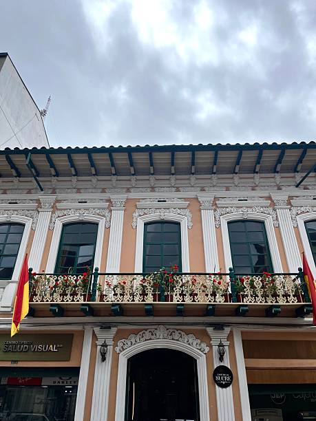 Cuenca, Azuay, Ecuador - April 10, 2025: Traditional colonial building adorned with vibrant flowers and Ecuadorian flags, showcasing the charm and architectural heritage of Cuenca, Ecuador, on a cloudy day