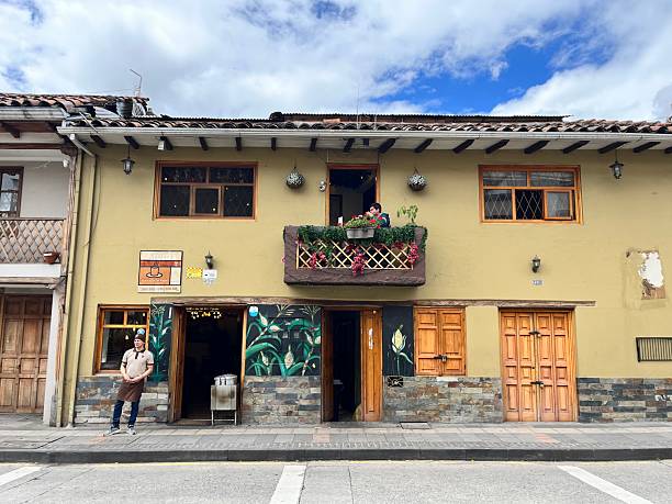 Cuenca, Azuay, Ecuador - April 10, 2025: Man enjoying a refreshing drink on a balcony of a traditional Ecuadorian building in Cuenca, while a waiter patiently waits outside the bustling restaurant below