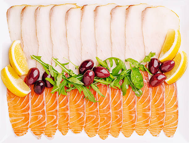 A beautifully arranged platter showcases thinly sliced salmon and turkey accompanied by fresh greens, olives, and lemon wedges. This colorful display is perfect for a casual gathering.