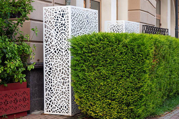 Stylish white decorative panels with a geometric pattern near clipped clumps of thuja trees near a building - perfect for architectural, landscape or design projects. Modern, clean, versatile.