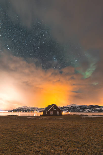 istock Aurora Borealis shimmers faintly through the clouds above a rustic red barn in Norway, with snow-dusted mountains and distant lights adding charm to the Arctic night 2230142864