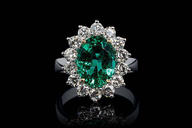 silver or gold ring with emerald stone and diamonds on black background close-up