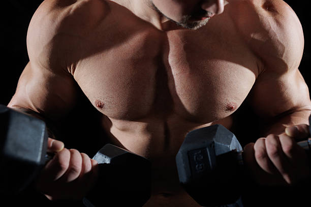 istock A male bodybuilder doing exercises with dumbbells on a black background. 2230143290