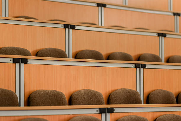 A spacious lecture hall featuring rows of empty, cushioned wooden seats. the arrangement provides a sense of order and anticipation, capturing the essence of academic settings.