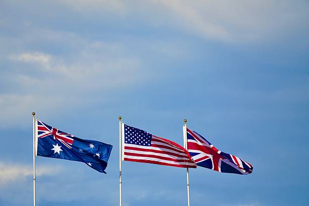 istock Australian, American, and British Flags Waving Against Blue Sky 2230151941
