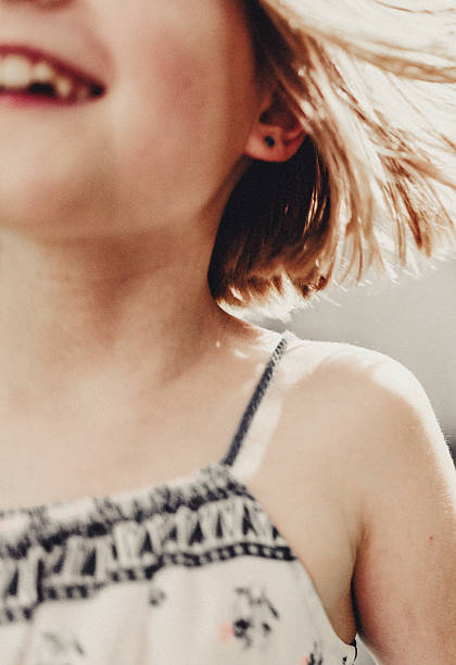 A bright summer moment in motion – the girl laughs with pure joy, her hair flying in the warm light. The cropped frame reveals only part of her face and shoulder, emphasizing the spontaneity and lightness of the moment.