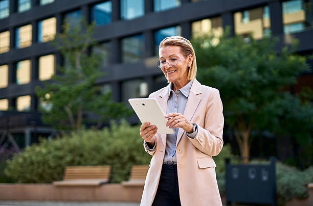 istock Smiling businesswoman using digital tablet in front of office building 2230163045