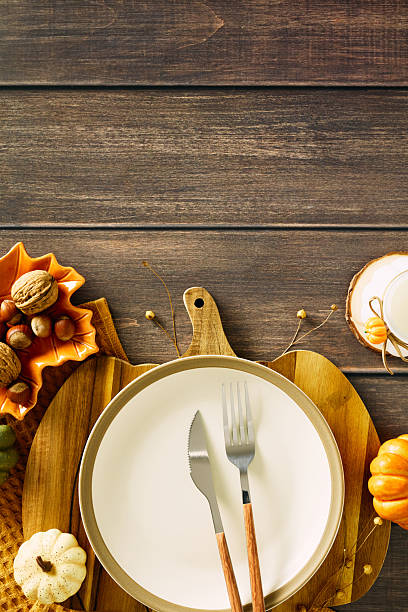 istock Vertical autumn table setting with empty plate, cutlery, pumpkins, nuts, and candle on rustic wooden background. 2230164746