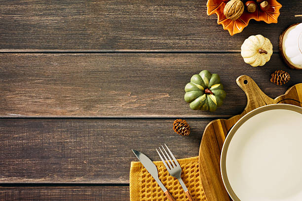 Rustic autumn table setting with empty plate, cutlery, pumpkins, nuts, and candle on wooden background. Perfect for Thanksgiving, harvest, or seasonal food themes.