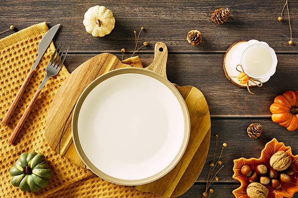 istock Top view of rustic autumn table setting with empty plate, pumpkins, nuts, candle, and cutlery on wooden background. 2230164923