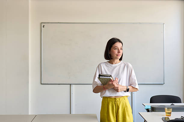 istock Young teacher holding notebooks and looking away in classroom 2230166674