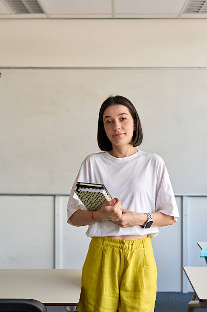 istock Young female teacher holding notebooks in classroom: ready for lecture 2230166818