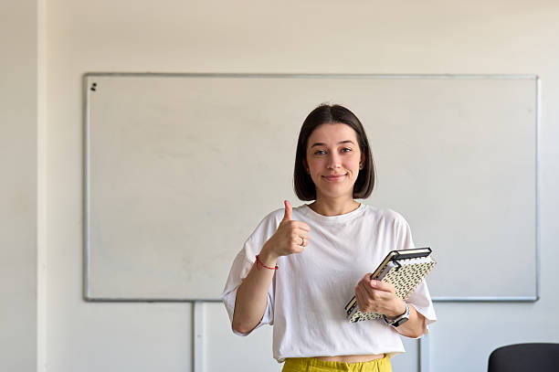 istock Young teacher gesturing thumbs up in classroom 2230166947
