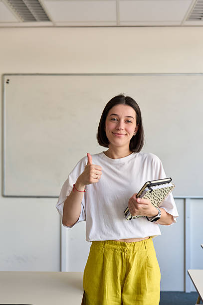 istock Young teacher gesturing thumbs up in classroom 2230167064