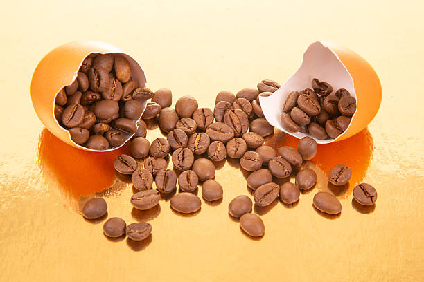 A broken egg with coffee beans spilling out on a golden surface, surrounded by scattered eggshells, creating a surreal and creative composition for food and beverage themes
