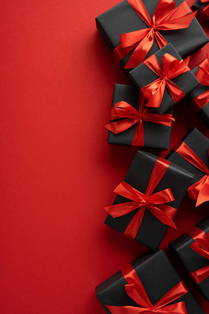 istock Multiple vertical black gift boxes with elegant red bows are displayed on a vibrant red surface, creating festive composition evoking feelings of celebration, joy, and special occasions 2230179520