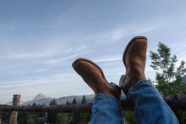 POV past ranchers feet on fence rail at sunrise, Canadian Rockies