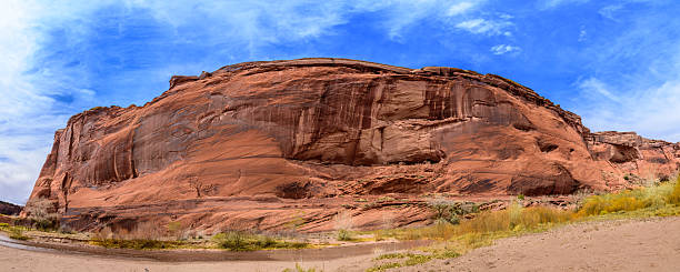 Canyon de Chelly National Monument, in northeastern Arizona, preserves nearly 5,000 years of human history within its dramatic sandstone walls. The canyon has been home to Ancestral Puebloans, known as the Anasazi, who built cliff dwellings here between 350 and 1300 CE, and to the Diné (Navajo) people who continue to live and farm within its sheltered valleys today. Carved by the forces of water and wind over millions of years, the canyon’s sheer cliffs rise to 1,000 feet above the canyon floor, revealing layers of ancient rock from the Permian period. From these rim overlooks, visitors can gaze down upon a living landscape where Navajo families maintain their traditions amidst towering formations, cottonwood groves, and sacred archaeological sites.  This scene was photographed from Canyon Road at Canyon de Chelly National Monument near Chinle, Arizona, USA.