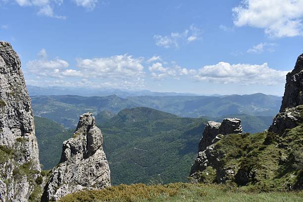 An awe-inspiring shot capturing the unique rock pinnacles and lush, forested valleys of the Pyrenees mountains. The foreground features textured, ancient stone and alpine scrub, leading the eye to a sprawling, majestic panorama. This image evokes feelings of freedom, exploration, and the raw power of nature. Perfect for travel blogs, environmental campaigns, and outdoor adventure publications