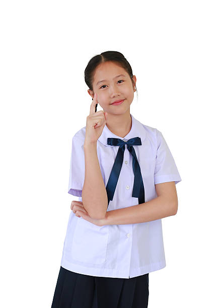 istock Smiling Asian student girl in primary or elementary school uniform pointing index finger up isolated on white studio background. 2230202896