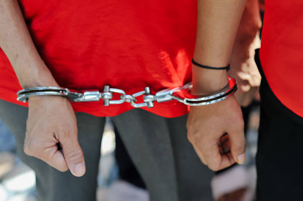 Close-up of a prisoner’s hands in handcuffs, wearing an orange jumpsuit. Concept of arrest, law enforcement, criminal justice, and incarceration.