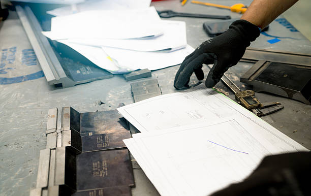 istock Worker's hand in black gloves examining technical drawings and metal tools on a workshop table, highlighting the precision and skill involved in industrial craftsmanship and manufacturing planning. 2230204088