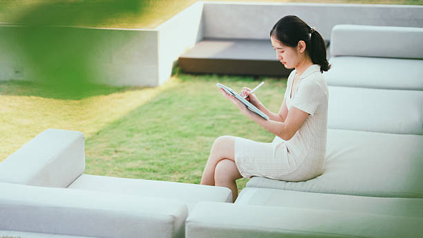 A Gen Z woman focuses on a tablet while sitting in the park, symbolizing flexibility in learning and working.  remote work, online class, digital workspace, tablet use, tech-savvy student, greenery, education tech.