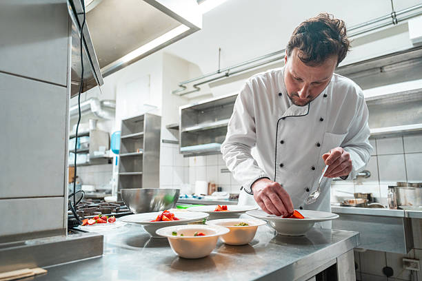 istock Professional Chef Carefully Plates Culinary Creation In Bright Industrial Kitchen 2230205536