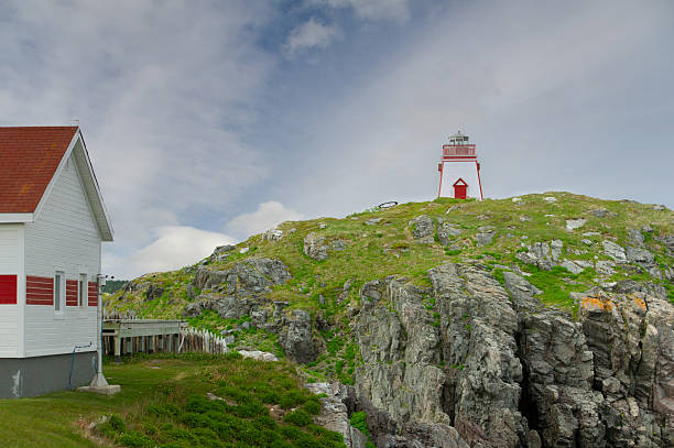 Fort Point lighthouse near Trinity, Newfoundland, standing on rugged coastal rocks under a clear blue sky.