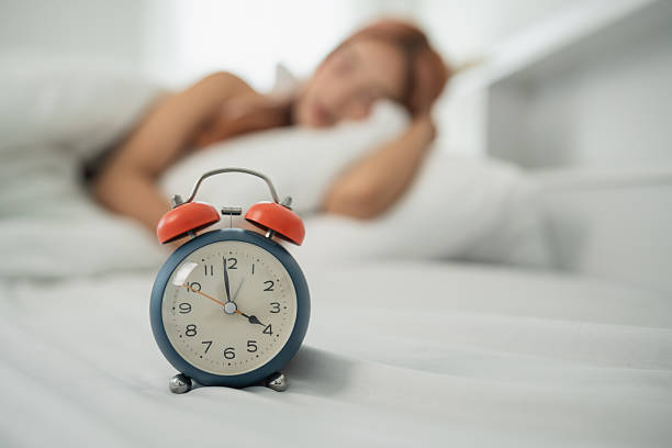 istock Alarm Clock on Bedside Table with Sleeping Woman in Soft Focus, Morning Routine and Time Management Concept in a Cozy Bedroom Setting 2230210009