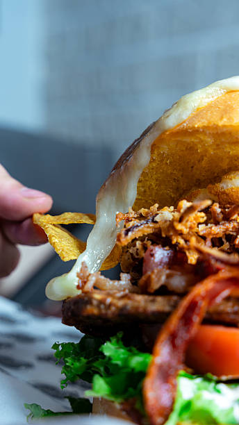 istock Hand dipping nacho chip into melted cheese on a loaded burger 2230212813