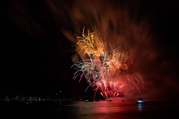 istock Vibrant fireworks explode over a calm water body, reflecting colorful lights in the night sky. 2230218542