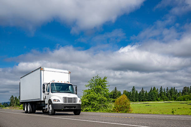 istock Compact middle duty day cab white rig semi truck transporting cargo in box trailer running on the local highway intersection 2230222420
