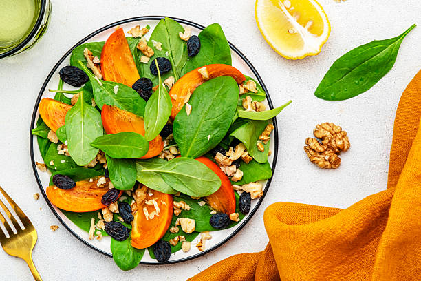 Autumn vegan persimmon salad with walnuts, blue raisin and spinach, white background, top view