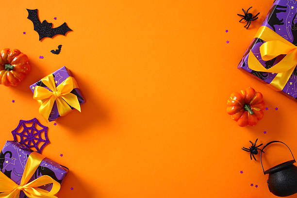 istock Halloween greeting card design. Flat lay composition with pumpkins, bats, spiders, cauldron, and gift boxes on orange background 2230224681