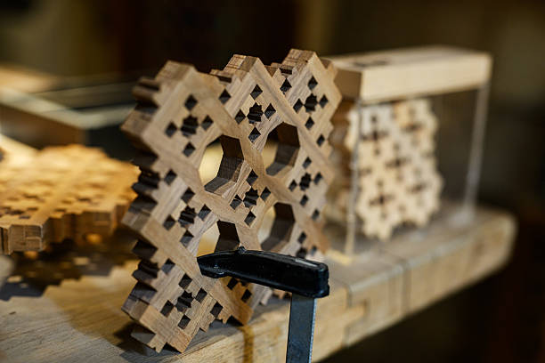 Handcrafted geometric lattice panels held in place with a clamp on a wooden workbench, highlighting artisanal woodworking techniques and Arabic design.