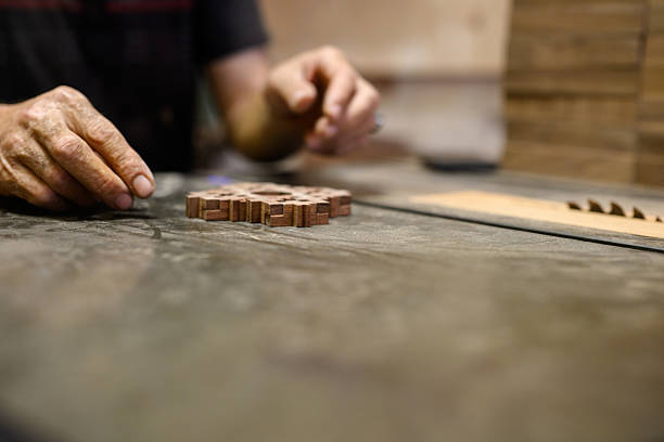 Closeup of carpenter’s hands arranging carved wooden lattice pieces on a flat workbench, highlighting traditional craftsmanship and precision.