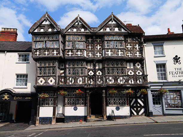 Ludlow, UK - Aug 09 2025: Front elevation of The Feathers, a Tudor half-timbered pub and hotel with ornate windows and flower baskets under a bright sky in Ludlow, Shropshire, England.