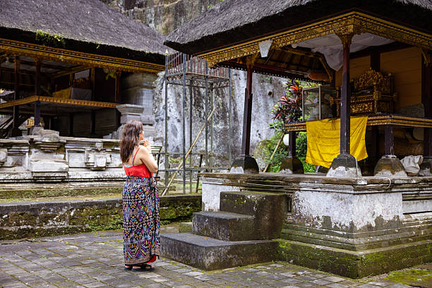 Side view of handsome female in hindu skirt praying and doing Namaste inside of Balinese temple in the jungle, Indonesia