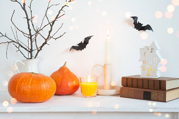 Halloween holiday decoration objects on bleached wooden table with glowing lights and white wall as background