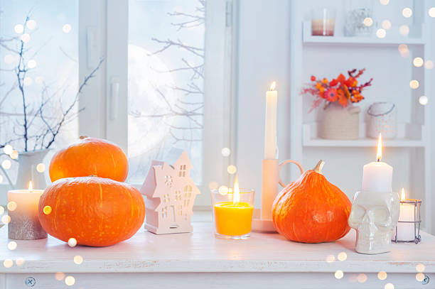 istock Bright pumpkins, burning candles and other Halloween holiday decoration objects on bleached wooden table in house room interior background with scary view from window 2230245341