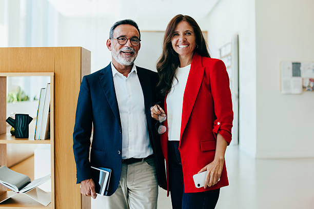 istock Two senior executives standing together and smiling in an office environment 2230245448